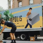 three men moving a fake plant out of a moving truck