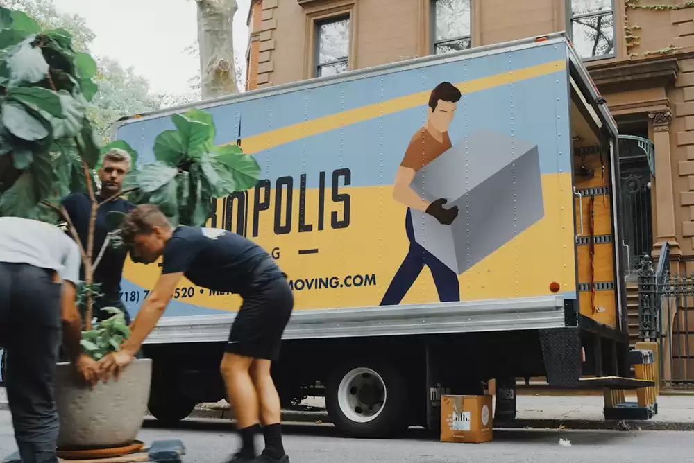 three men moving a fake plant out of a moving truck